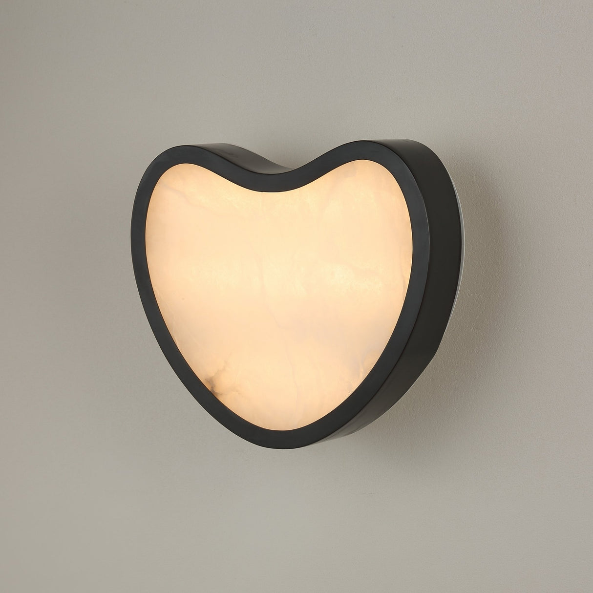 Niori Marea LED wall light in matte black with a teardrop-shaped natural alabaster panel set in a curved copper frame, shown lit against a light grey wall.