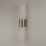 Niori Fiora LED alabaster wall light with two vertical cylindrical columns joined by a satin nickel band, mounted on a plain light wall.