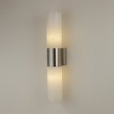 Niori Fiora LED alabaster wall light with two vertical stone cylinders joined by a satin nickel band, casting warm light on a neutral wall.