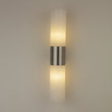 Niori Fiora LED wall light illuminated on a neutral wall, showing two alabaster cylinders glowing warm white above and below a satin nickel band.