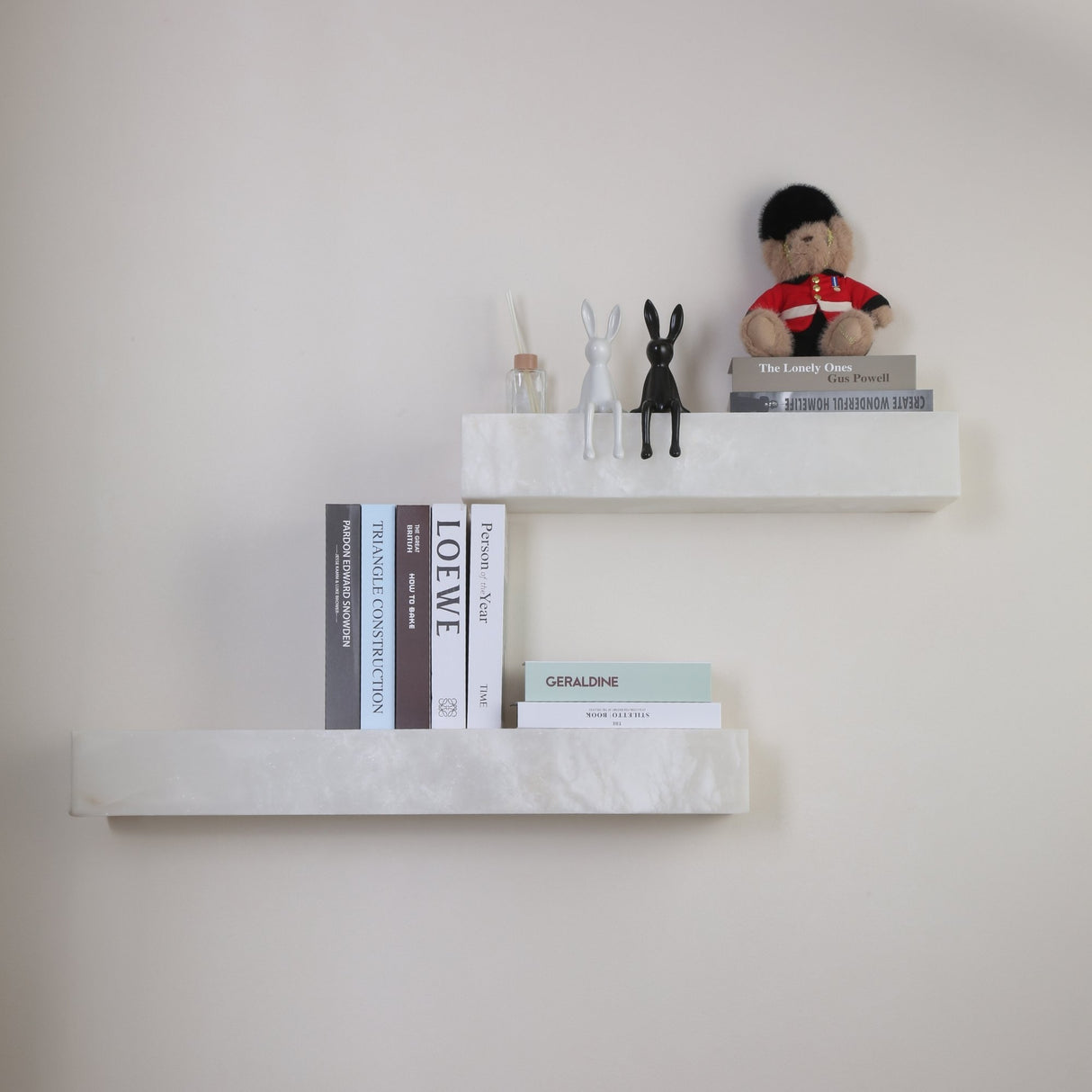 Niori Kate Small LED alabaster wall shelf light in soft white, styled with books, rabbit figurines and a guardsman bear on a neutral wall.