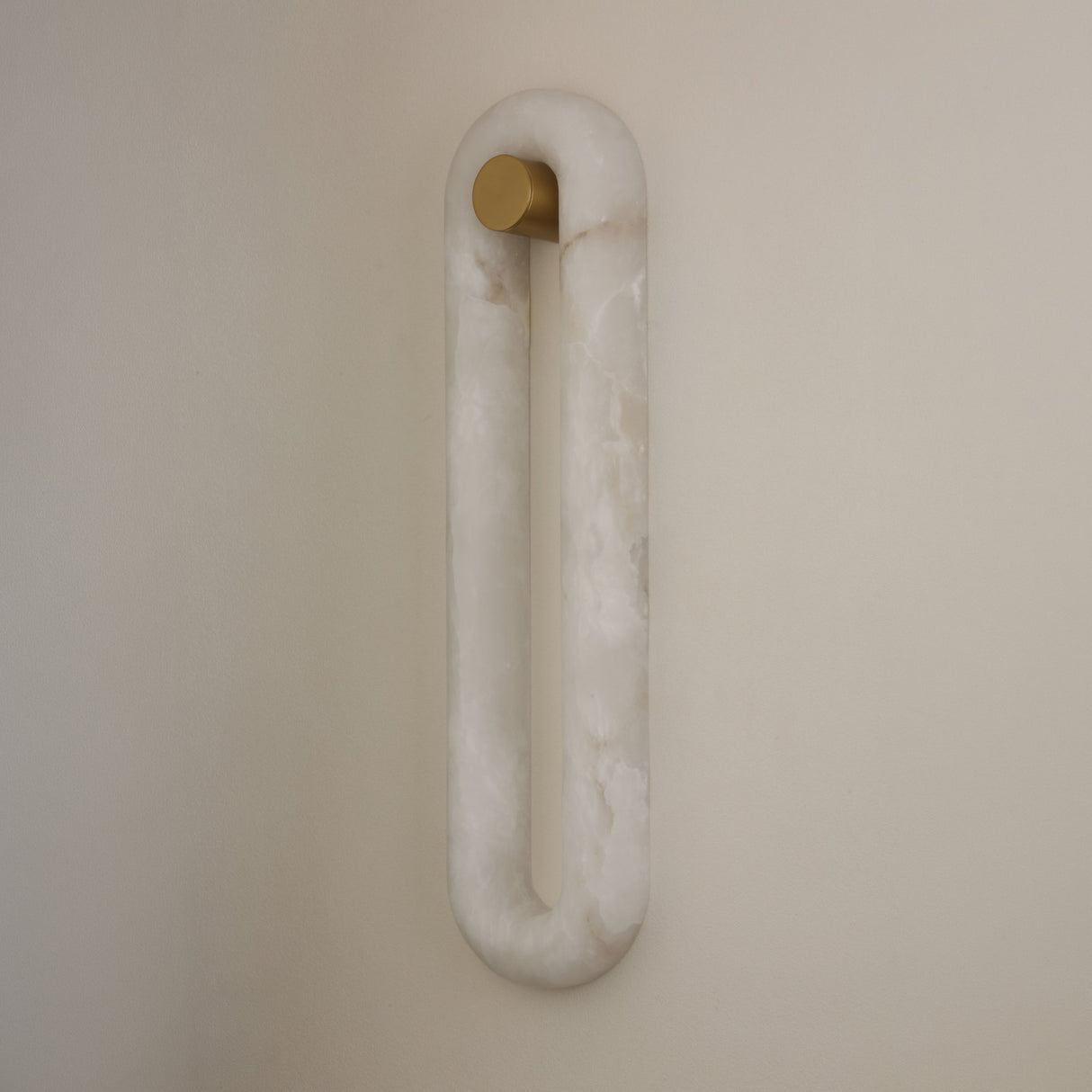 Niori Serava Small alabaster wall light with a vertical oval stone ring and matt black cylindrical fixing, mounted on a pale wall.