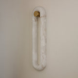 Serava LED Alabaster Wall Light Large in soft white, an elongated oval loop with brushed brass mounting bracket, mounted on a plain neutral wall.