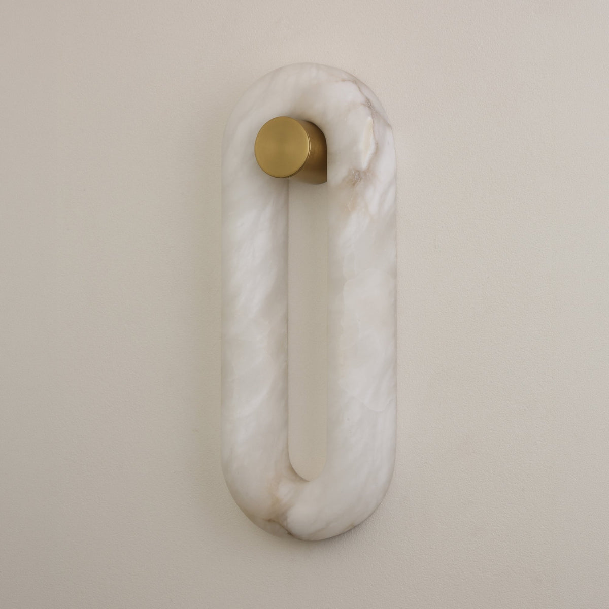 Serava LED Small Alabaster Wall Light in soft white, oval ring shape with natural alabaster veining and a brushed brass cylindrical fixing, mounted on a plain light wall.