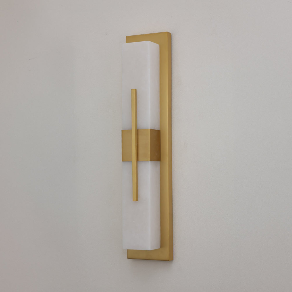 Niori Caldera Large LED wall light with a tall Spanish alabaster column, brushed brass backplate and vertical brass band, shown against a pale wall.