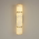 Niori Almora LED alabaster cylinder wall light in brass, illuminated with warm up and down glow, mounted on a light grey wall.