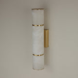 Niori Almora LED alabaster cylinder wall light in a medium size, with brass banding and rectangular brushed brass wall plate on a neutral wall.
