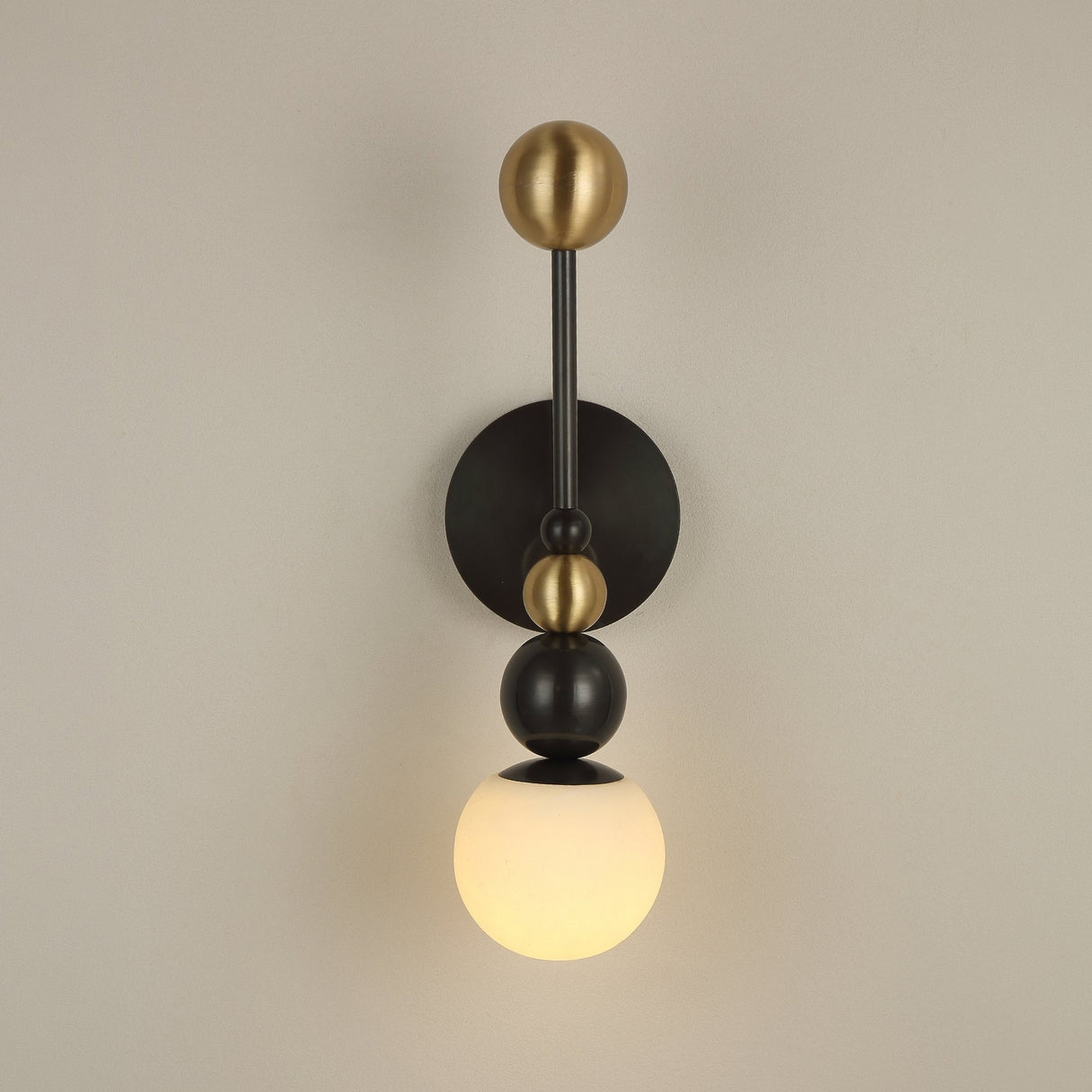 Niori Zeal Vertical Orb wall light with stacked brushed brass and matt black spheres above an illuminated alabaster globe, on a neutral wall.