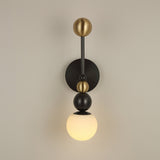 Niori Zeal Vertical Orb wall light with stacked brushed brass and matt black spheres above an illuminated alabaster globe, on a neutral wall.