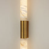 Eryon LED Large alabaster wall light with two cylindrical stone columns joined by a brushed brass mount and ribbed bronze centre sleeve, illuminated.