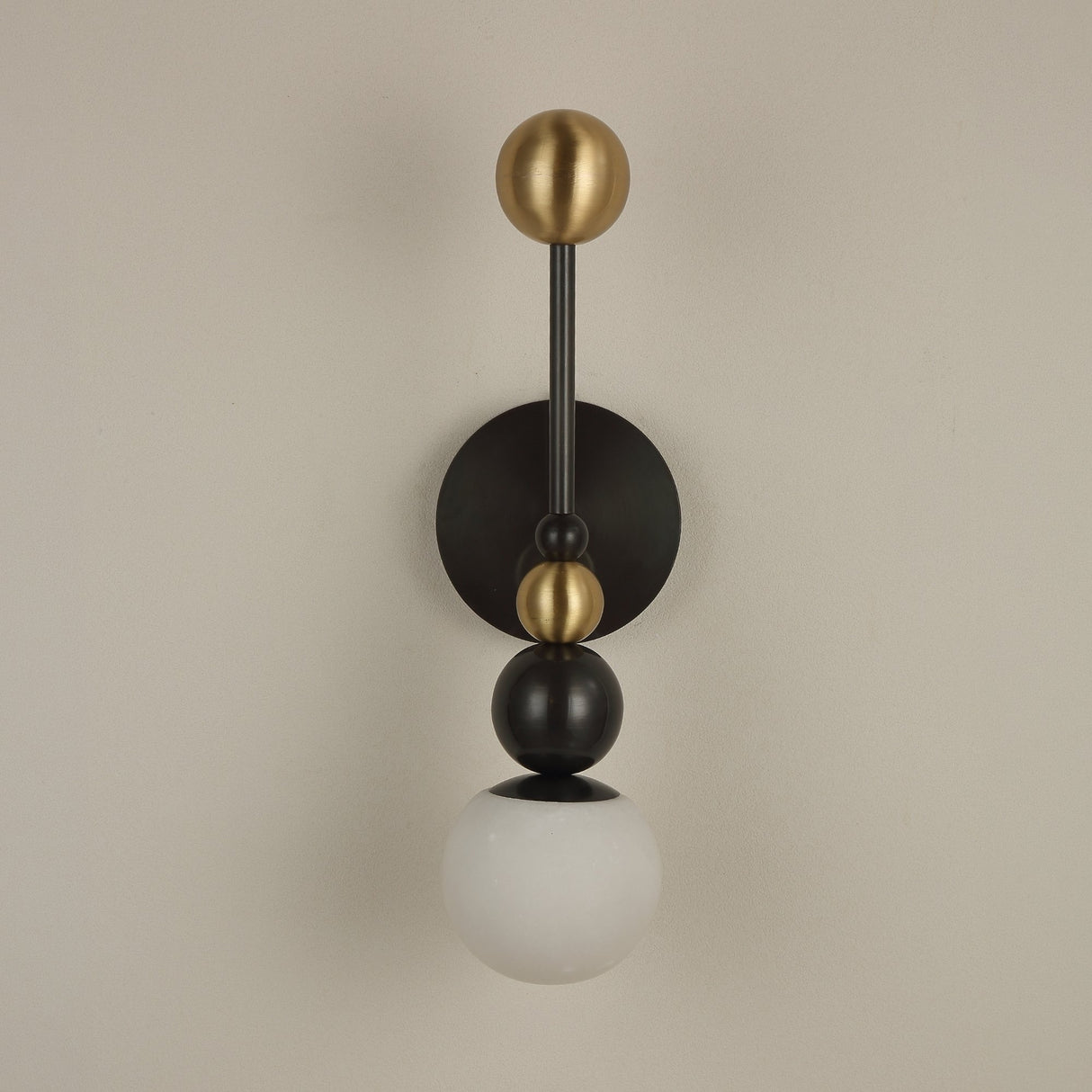 Niori Zeal Vertical Orb wall light with stacked brushed brass and matt black spheres above a glowing alabaster globe, on a neutral wall.