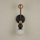 Niori Zeal Vertical Orb wall light with stacked brushed brass and matt black spheres above a glowing alabaster globe, on a neutral wall.