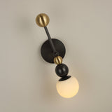Niori Zeal Vertical Orb wall light with stacked brass and matt black spheres above a glowing alabaster globe, mounted on a neutral wall.