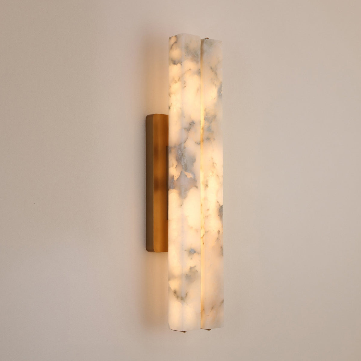 Selvara LED Large Alabaster Double Wall Light in Brushed Brass, two vertical alabaster columns glowing warm white on a slim brass backplate, mounted on a plain light wall.