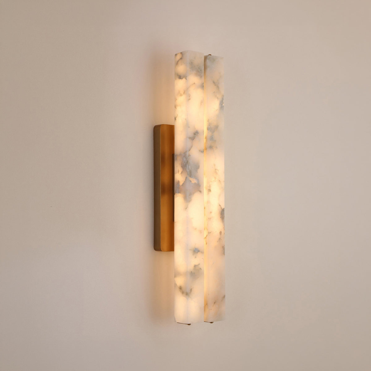 Selvara LED Medium Alabaster Double Wall Light with two vertical alabaster bars glowing warm white, mounted on a brushed brass backplate against a plain light wall.