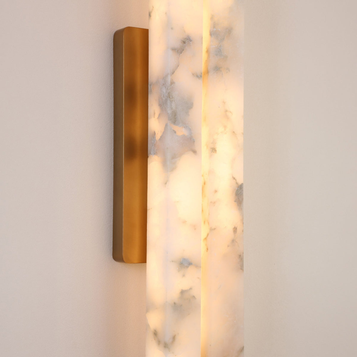 Selvara LED Large Alabaster Double Wall Light with brushed brass backplate, close-up of two illuminated alabaster columns showing natural grey-white veining against a plain wall.