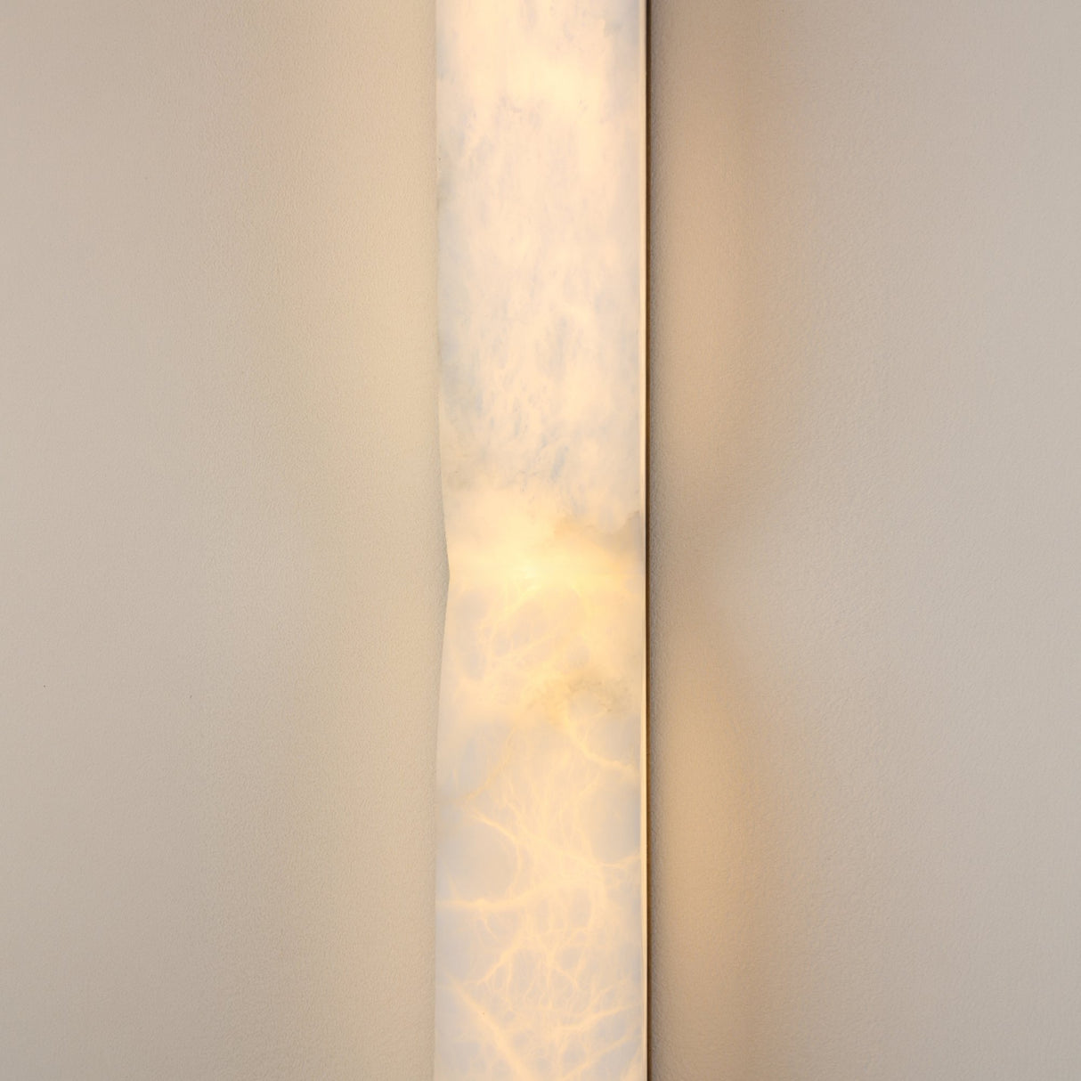 Vera Large LED Alabaster Wall Light in soft white, a vertical natural stone column with a sculpted inward contour, glowing warmly against a neutral wall.