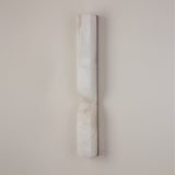 Vera Large LED alabaster wall light, a tall vertical column with a sculpted inward waist, natural white stone finish with a slim brass edge, mounted on a plain light wall.