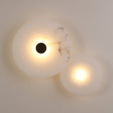 Solmira LED Dual Disc Alabaster Wall Light with overlapping large and small alabaster discs, brushed brass centre detail, and warm white glow, mounted on a plain light wall.