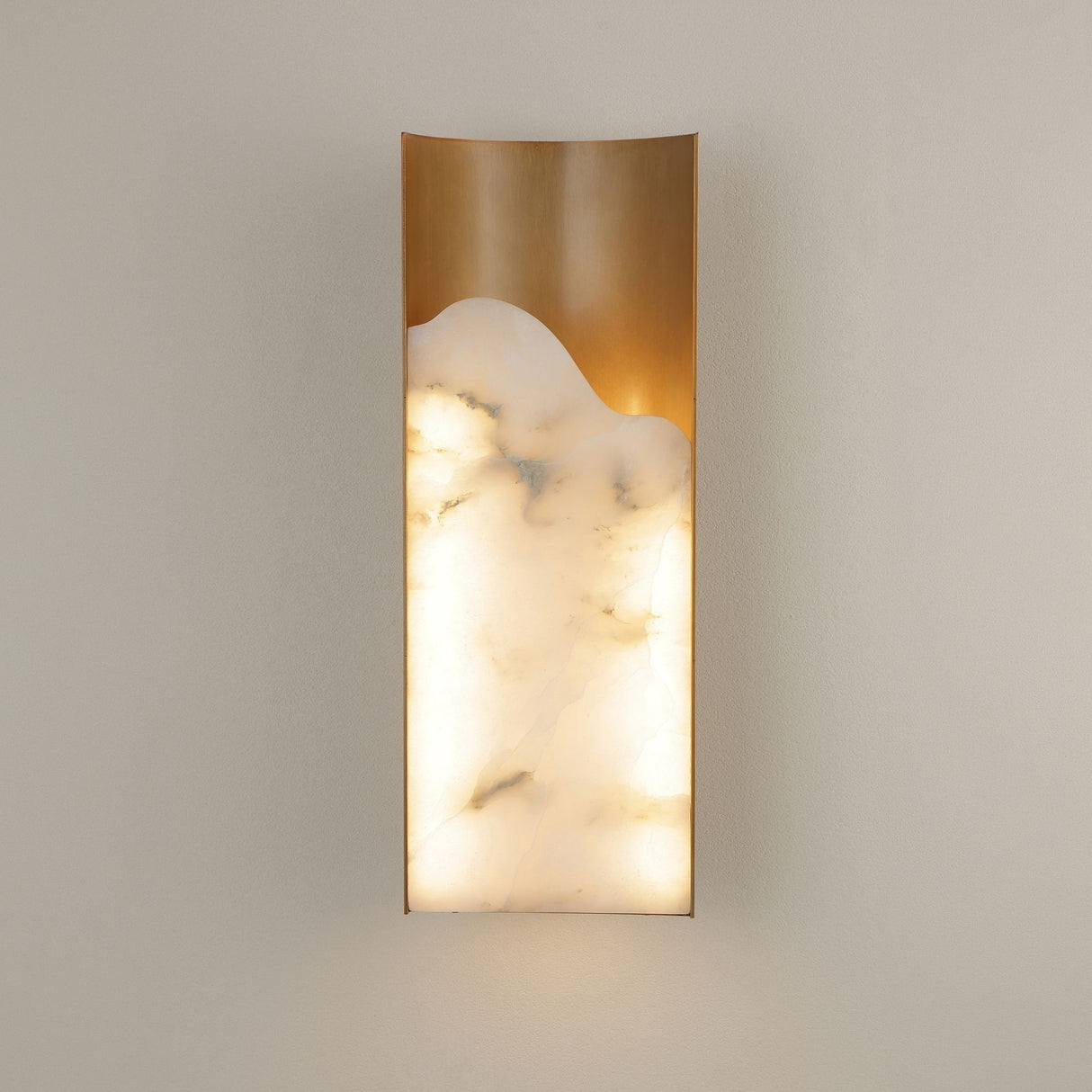 Caelith LED Medium carved alabaster wall light by Niori with brushed brass frame and warm-lit natural Spanish alabaster panel mounted on a light wall.