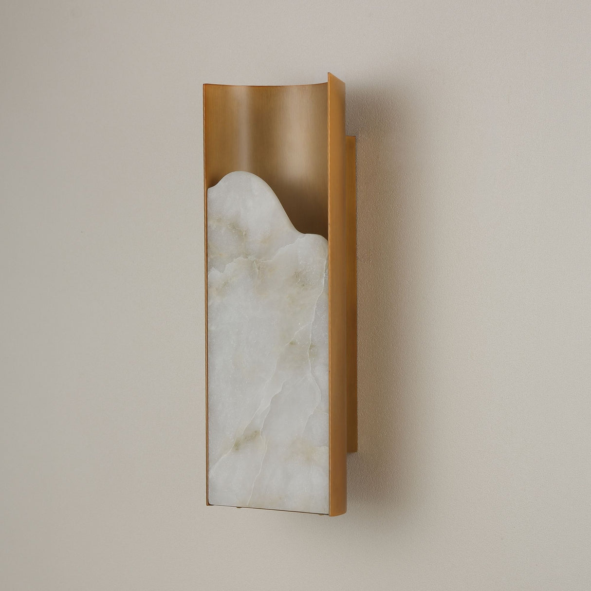 Niori Caelith Medium wall light shown at an angle, with a carved natural alabaster slab set in a brushed brass frame against a neutral wall.