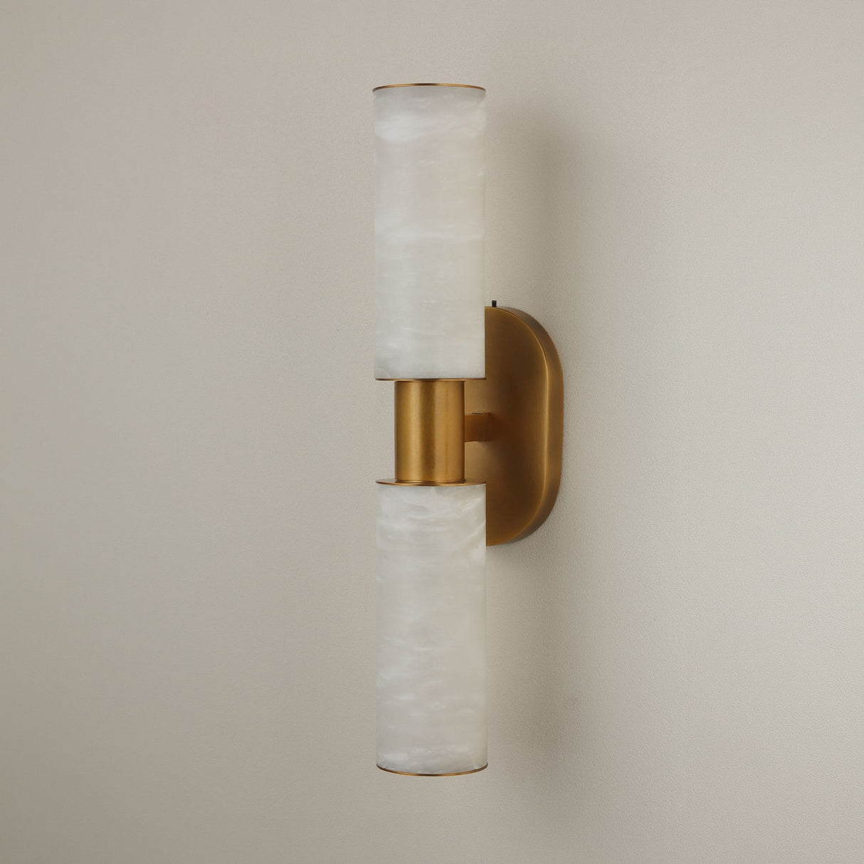 Niori Lumara 2 light twin tube wall light with stacked Spanish alabaster cylinders and brushed brass collar and backplate, on a pale wall.