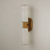 Niori Lumara 2 light twin tube wall light with stacked Spanish alabaster cylinders and brushed brass collar and backplate, on a pale wall.