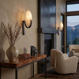 Mica 1 Light Disc Alabaster Wall Light in matt black, illuminated on a living room wall beside a stone fireplace with mountain views.