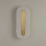 Niori Averra Small LED wall light with capsule-shaped Spanish alabaster body and central brass spine, mounted on a neutral wall.