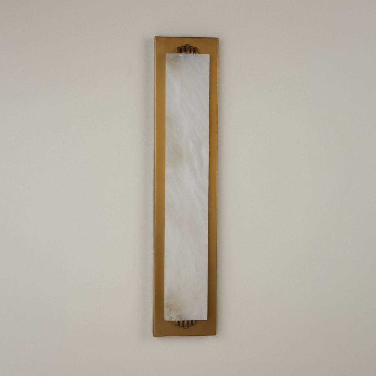 Niori Valora vertical wall light with a tall natural alabaster panel set in a brushed brass rectangular backplate, mounted on a pale neutral wall.