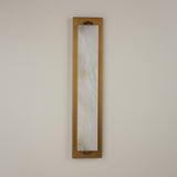 Niori Valora vertical wall light with a tall natural alabaster panel set in a brushed brass rectangular backplate, mounted on a pale neutral wall.