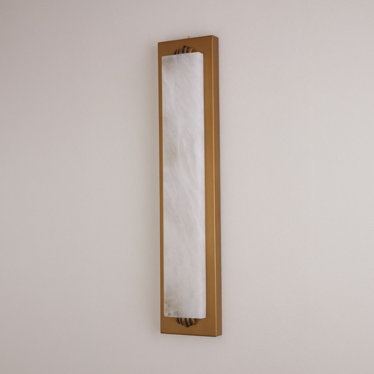 Niori Valora vertical wall light with tall natural alabaster panel in a slim brushed brass rectangular frame, mounted on a pale neutral wall.