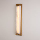 Valora vertical alabaster wall light illuminated on a pale wall, showing natural stone veining within a slim brushed brass rectangular frame.
