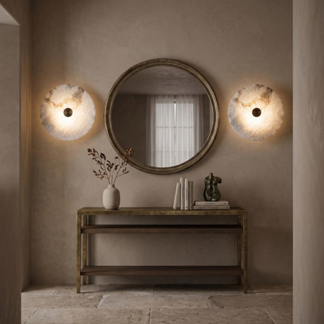 Pair of Cerchio round alabaster wall lights with brass centre boss, mounted either side of a round mirror above a wood and brass console table in a hallway.