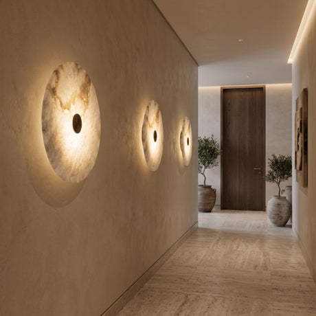 Cerchio LED Round Alabaster Wall Light, 30cm circular stone disc with central brass boss, shown lit in a row of three along a hallway wall.