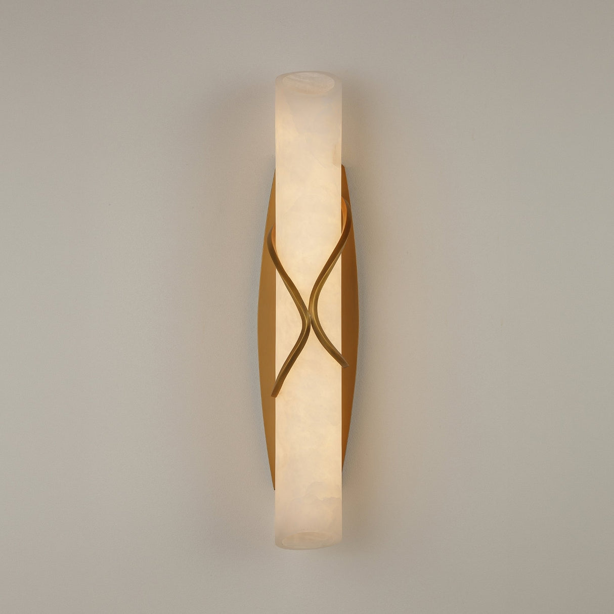 Valora LED Alabaster Wall Light in brushed brass, a vertical alabaster column wrapped by crossing brass bands, glowing warm white on a plain light background.