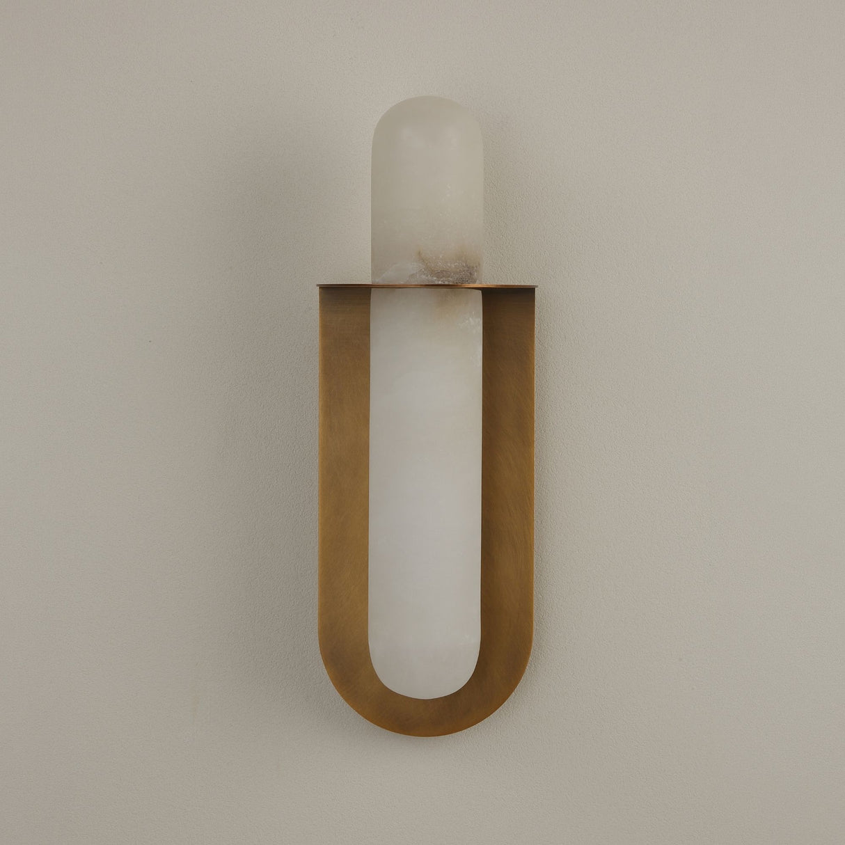 Niori Luneth Large wall light with a vertical natural alabaster rod cradled in a brushed brass U-shaped backplate, mounted on a pale wall.