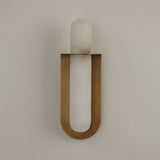 Niori Luneth Large wall light with a vertical natural alabaster rod cradled in a brushed brass U-shaped backplate, mounted on a pale wall.