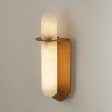Niori Luneth Small alabaster wall light with a vertical white stone column set in a curved brushed brass cradle, shown lit against a pale wall.
