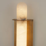 Niori Luneth Large wall light with a vertical Spanish alabaster rod in a brushed brass U-shaped backplate, illuminated in warm white against a pale wall.
