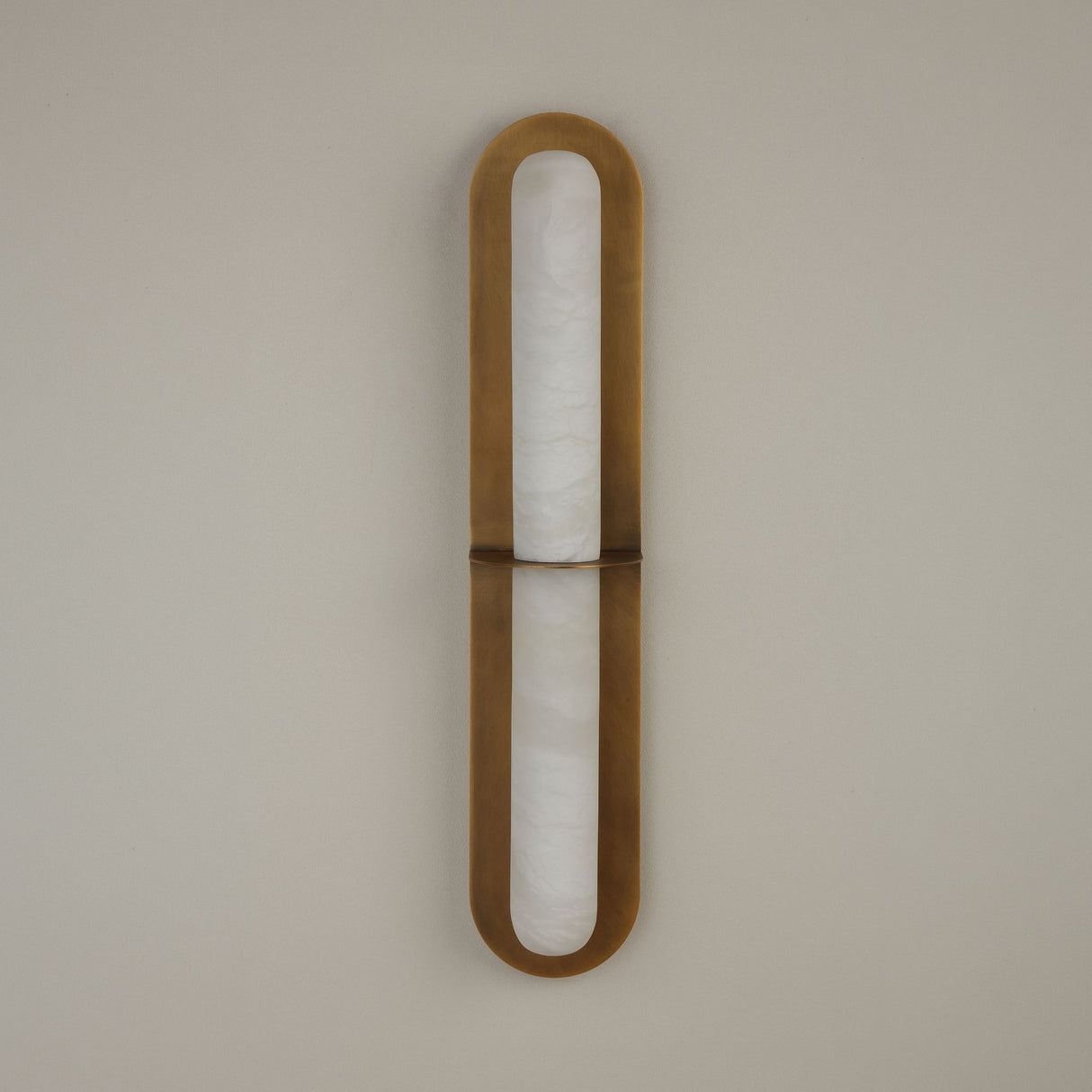 Niori Eliora LED wall light with vertical alabaster column framed by a brushed brass rounded surround, divided by a central bar, on a pale wall.