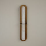 Niori Eliora LED wall light with vertical alabaster column framed by a brushed brass rounded surround, divided by a central bar, on a pale wall.