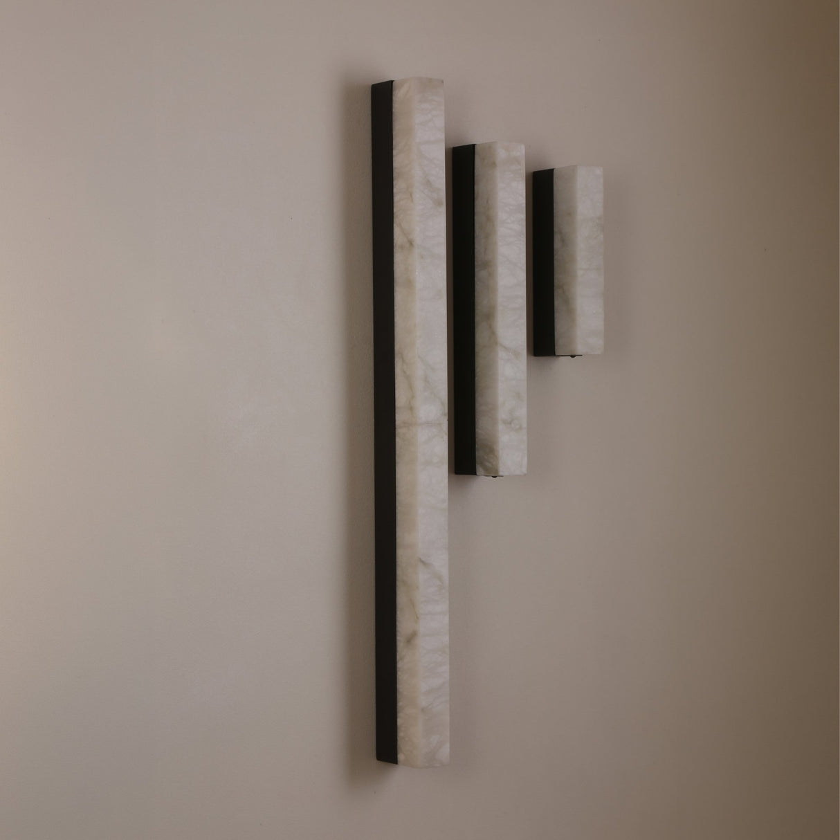 Three Niori Cornova LED slim linear alabaster wall lights in varying heights with matte black frames, mounted vertically on a neutral wall.