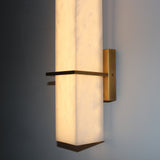Aurevon LED Alabaster Vertical Panel Wall Light in Brushed Brass, close-up of the illuminated stone panel and horizontal brass arm against a grey wall.