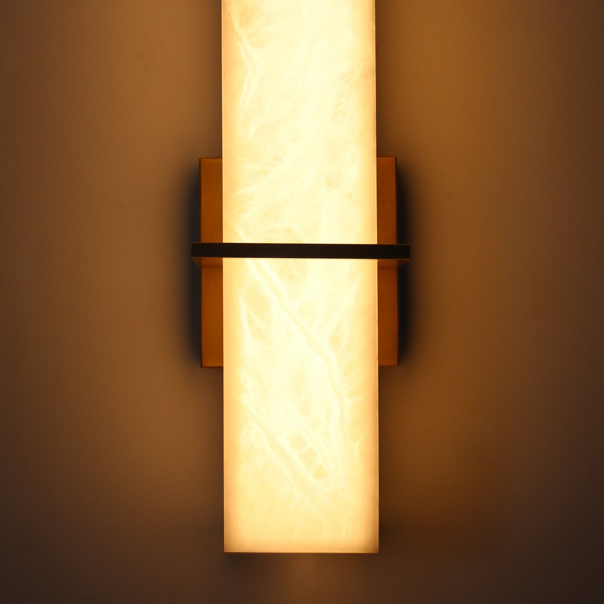 Aurevon LED Alabaster Vertical Panel Wall Light in Brushed Brass, glowing warm white with a slim brass crossbar, shown illuminated on a dark wall.