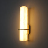 Aurevon LED alabaster vertical panel wall light with brushed brass backplate and slim horizontal arm, glowing warm white against a dark background.