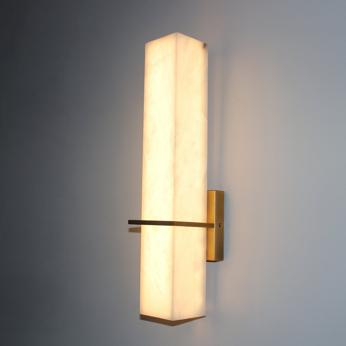 Aurevon LED alabaster vertical panel wall light with brushed brass backplate and horizontal arm, glowing warm white against a grey background.