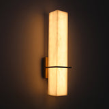 Aurevon LED alabaster vertical panel wall light with brushed brass backplate and bar, glowing warm white against a dark background.