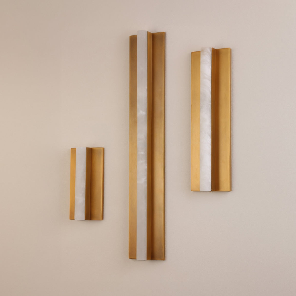 Elvaris Small vertical wall light with alabaster column between brushed brass panels, shown alongside two larger versions on a plain wall.