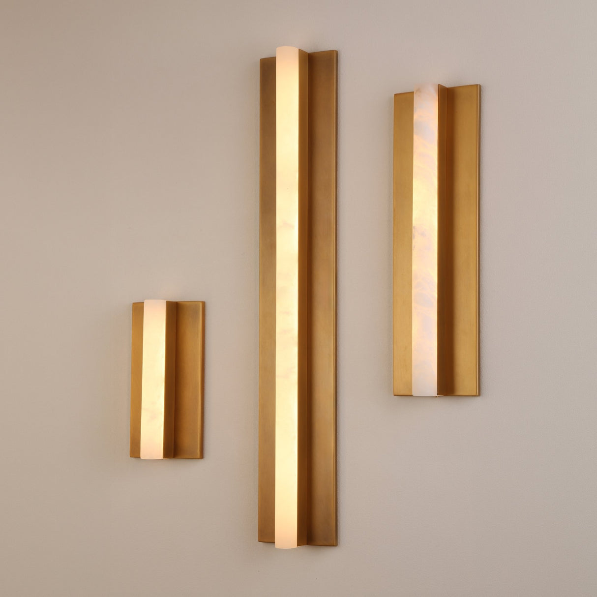 Elvaris Small vertical LED wall light with warm-lit alabaster column between brushed brass panels, shown among two larger sizes on a light wall.